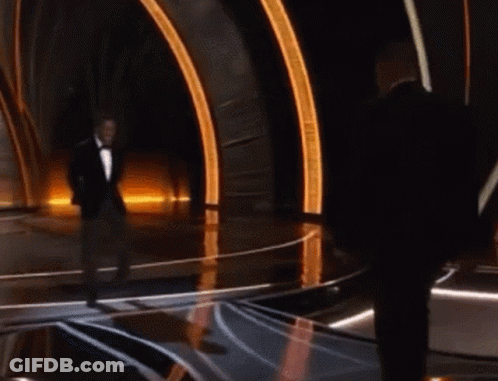 A Man In A Tuxedo Stands On A Stage With Another Man GIF