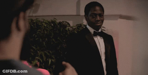 A Man In A Tuxedo Talks To Another Man In A Pink Shirt GIF
