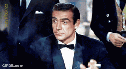 A Man In A Tuxedo With A Bow Tie Is Standing In Front Of A Sign That Says Cravello2022 GIF
