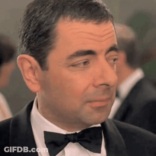 A Man In A Tuxedo With A Bow Tie Looks At The Camera GIF