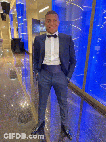 A Man In A Tuxedo With His Hands In His Pockets Stands In Front Of A Wall That Says ' The ' On It GIF