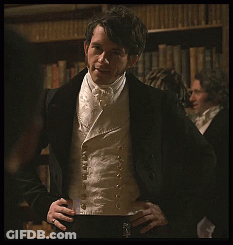 A Man In A Tuxedo With His Hands On His Hips Stands In Front Of A Bookshelf GIF