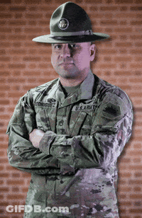 A Man In A U.s. Army Uniform Stands With His Arms Crossed In Front Of A Brick Wall GIF