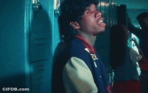 A Man In A Varsity Jacket Is Standing In Front Of Lockers GIF