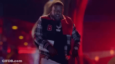 A Man In A Varsity Jacket Is Standing In Front Of The Word Pop It GIF