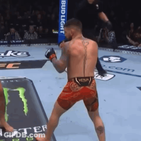 A Man In A Venum Shorts Stands In Front Of A Bud Light Sign GIF
