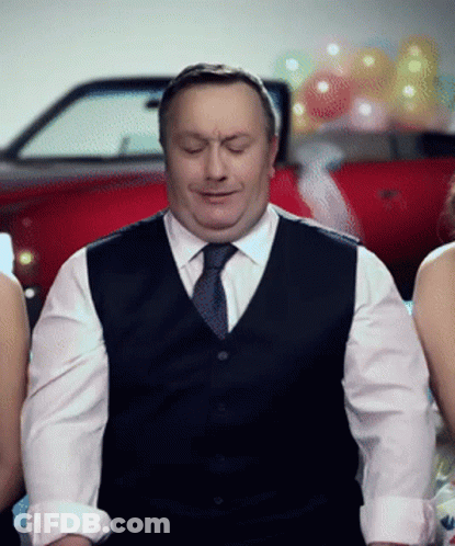 A Man In A Vest And Tie Is Sitting In Front Of Two Women GIF