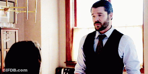 A Man In A Vest And Tie Is Standing In Front Of A Window GIF