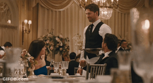 A Man In A Vest Is Carrying A Silver Tray To A Woman In A Blue Dress GIF