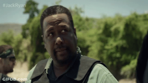 A Man In A Vest Stands In Front Of Trees With The Hashtag #Jackryan On The Bottom Right GIF