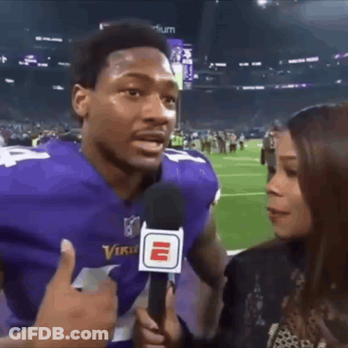 A Man In A Vikings Jersey Is Being Interviewed By A Woman . GIF