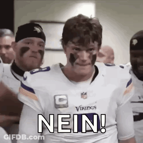 A Man In A Vikings Jersey Is Standing In Front Of A Group Of Men With Face Paint On Their Faces . GIF