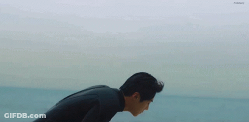 A Man In A Wetsuit Is Bending Over In The Ocean GIF