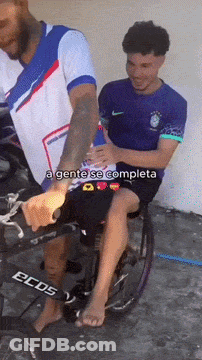A Man In A Wheelchair Is Being Helped By A Man In A Nike Shirt GIF
