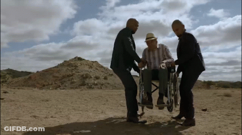 A Man In A Wheelchair Is Being Pushed By Two Men In The Desert GIF