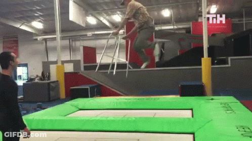 A Man In A Wheelchair Is Jumping On A Green Trampoline With The Letters Th Visible In The Background GIF