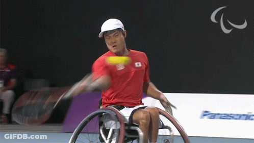 A Man In A Wheelchair Swings A Tennis Racket At A Tennis Ball GIF