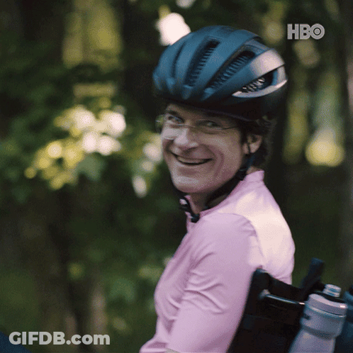 A Man In A Wheelchair Wearing A Helmet And A Pink Shirt With Hbo Written On The Bottom Right GIF