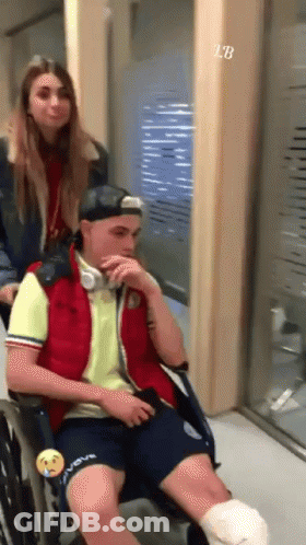 A Man In A Wheelchair With A Bandage On His Leg Is Being Pushed By A Girl GIF