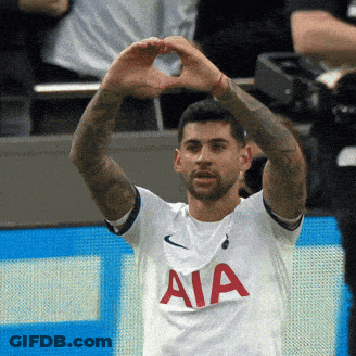 A Man In A White Aia Shirt Makes A Heart Shape With His Hands GIF