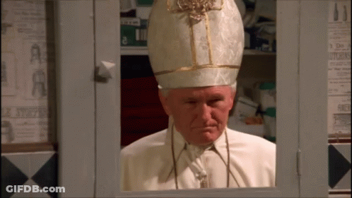 A Man In A White And Gold Hat Is Looking Out Of A Window GIF