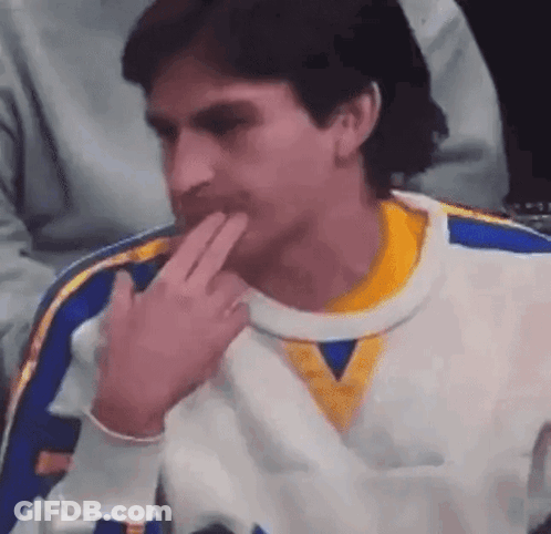 A Man In A White And Yellow Sweater Is Sitting In A Chair With His Hand On His Chin . GIF