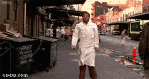 A Man In A White Apron Is Walking Down A Street In Front Of A Dumpster That Says Spit GIF