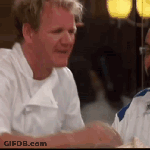 A Man In A White Chef 'S Coat Is Sitting At A Table With A Woman . GIF