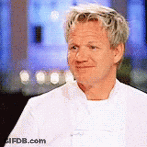 A Man In A White Chef 'S Coat Is Smiling And Looking Away From The Camera . GIF