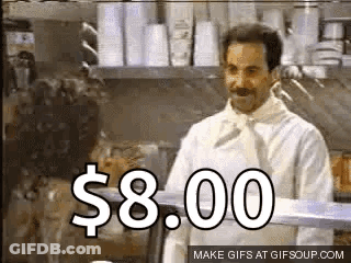 A Man In A White Chef 'S Coat Is Standing In A Kitchen With A Sign That Says $ 8.00 On It . GIF