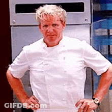 A Man In A White Chef 'S Jacket Is Standing With His Hands On His Hips In Front Of A Refrigerator . GIF