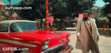 A Man In A White Coat And A Beard Is Standing Next To A Red Car . GIF