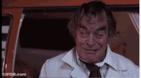 A Man In A White Coat And Tie Is Smiling And Looking At The Camera GIF