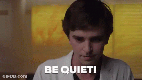 A Man In A White Coat Is Saying `` Be Quiet '' While Standing In Front Of A Window . GIF