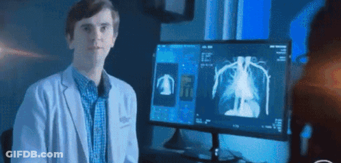 A Man In A White Coat Is Standing In Front Of A Computer Monitor . GIF