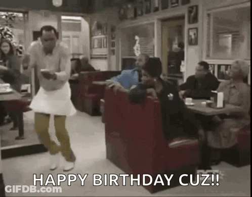 A Man In A White Dress Is Dancing In A Diner While A Woman Sits At A Table . GIF