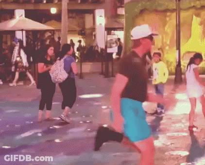 A Man In A White Hat And Blue Shorts Is Running In A Crowded Street GIF