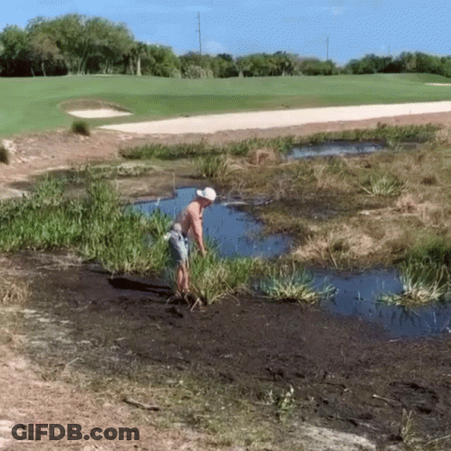 A Man In A White Hat Is Standing In A Puddle Of Water Near A Golf Course GIF