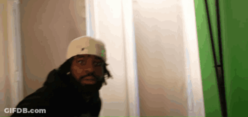A Man In A White Hat Is Standing In Front Of A Green Screen . GIF