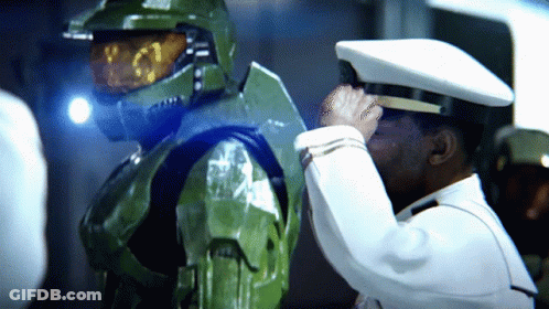 A Man In A White Hat Salutes Another Man In A Green Suit GIF