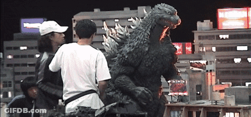 A Man In A White Hat Stands In Front Of A Giant Monster GIF