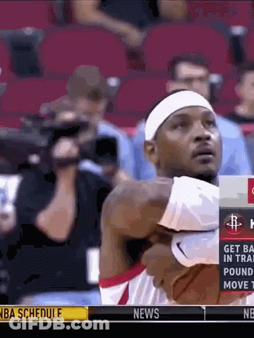 A Man In A White Headband Is Holding A Basketball In Front Of A Nba Schedule Advertisement GIF