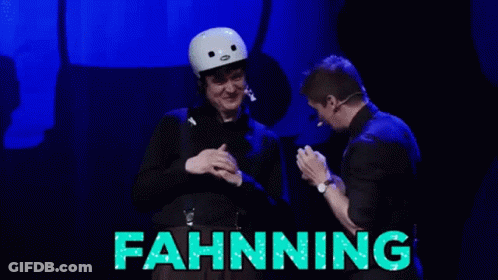 A Man In A White Helmet Stands Next To A Man In A Black Suit With The Word Fahnning Written In Green GIF