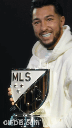 A Man In A White Hoodie Holds A Trophy That Says Mls GIF