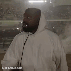 A Man In A White Hoodie Is Holding A Microphone In Front Of A Crowd . GIF