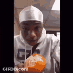 A Man In A White Hoodie Is Holding An Orange In His Hand . GIF