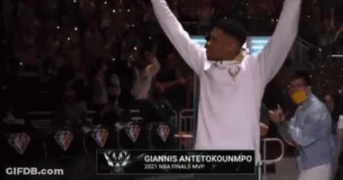 A Man In A White Hoodie Is Raising His Arms In The Air In Front Of A Crowd . GIF