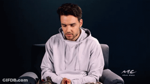 A Man In A White Hoodie Is Sitting In A Chair With A Mc Logo In The Background GIF