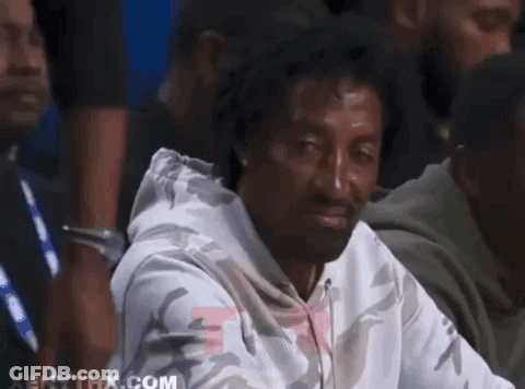 A Man In A White Hoodie Is Sitting In A Crowd And Making A Funny Face . GIF