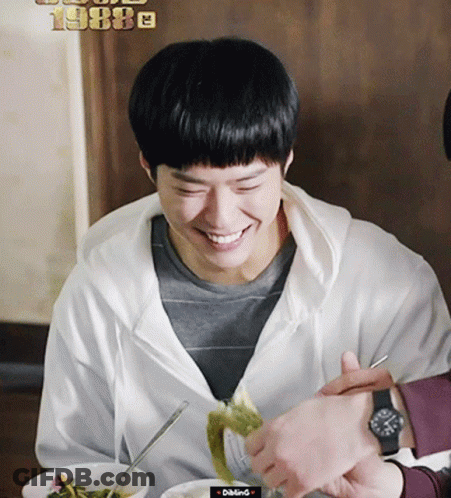 A Man In A White Hoodie Is Smiling While Eating A Meal GIF